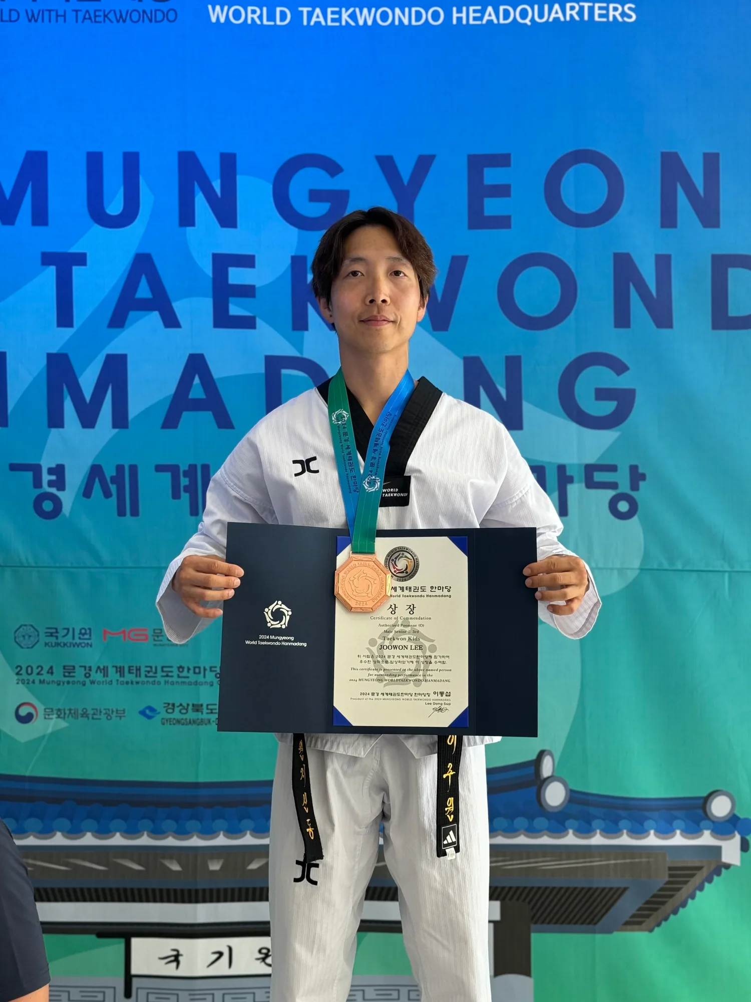 Master Joowon Lee holding his 2024 Mungyeong World Taekwondo Hanmadang certificate of commendation and bronze medal